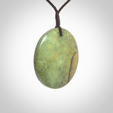 This piece is a large sized, oval round, disc pendant. It is suspended on a chocolate brown coloured braided cord that is length adjustable.